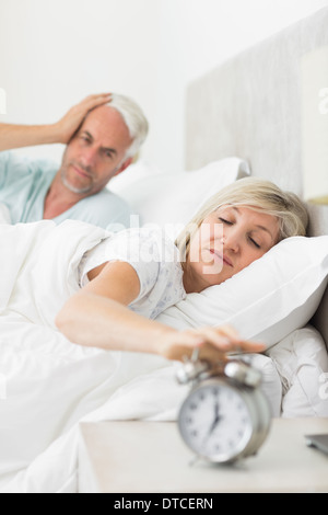 Manndeckung Ohren während Frau Hand mit Wecker im Bett ausstrecken Stockfoto