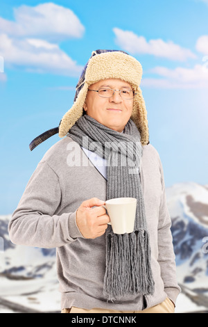 Ältere Mann hält eine Tasse Tee vor schneebedeckten Berg Stockfoto