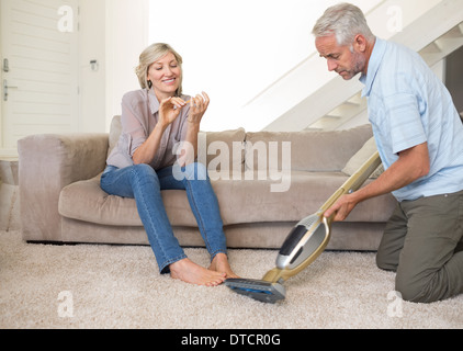 Frau Einreichung Nägel während Mann Staubsaugen Bereich Teppich Stockfoto