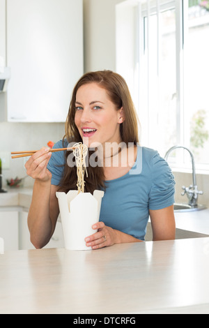 Lächelnde junge Frau essen Nudeln in Küche Stockfoto