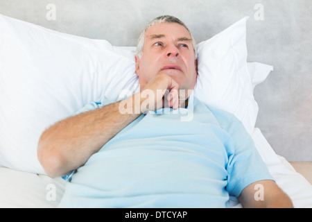 Nachdenklicher senior Mann im Bett liegend Stockfoto