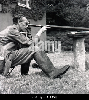 1950er Jahre, historisches Bild eines Gutsverwalters, der draußen auf einem kleinen Sitz sitzt und mit einem langen Teleskop die Aktivität von Tieren auf dem umliegenden Gelände beobachtet, England, Großbritannien. Stockfoto
