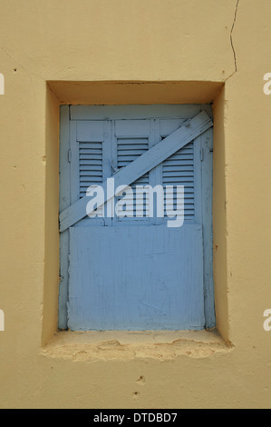 Blaue Fenster Shutter und gelbe rissige Wand. Verlassenes Haus außen vernagelt. Stockfoto