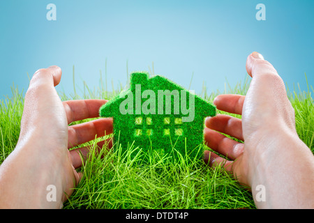 Eco House in Grasgrün, geschützt von Menschenhand auf blauem Hintergrund. Stockfoto