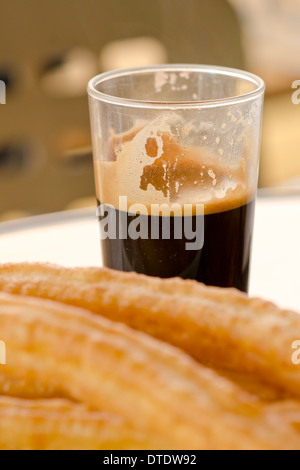 Tasse schwarzer spanischer Kaffee hinter einigen Churros (Porra) auf einem weißen Teller, ohne Zuckerzusatz. Andalusien, Spanien. Stockfoto