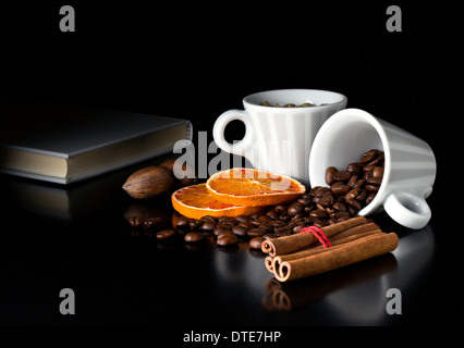 natürliche Kaffeebohnen mit Früchten und Buch am schwarzen Tisch Stockfoto