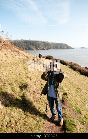 Ein kleiner Junge, der auf einem Küstenpfad spazieren geht, blickt mit einem Fernglas in den Himmel, während er in der Nähe von Dartmouth in Devon, Großbritannien, unterwegs ist Stockfoto