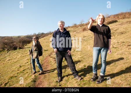 Grauhaarige Vater und seinen zwei Söhnen, die im Teenageralter in Wanderschuhe heraus auf einem Küstenweg gehen Sie über die Landschaft auf der Suche nach einem sonnigen Tag in Devon Stockfoto