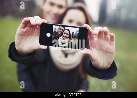 Zärtlich junges Paar unter einem Selbstporträt mit einem Smartphone im Park. Gemischte Rassen Teenager Mann und Frau im Freien. Stockfoto