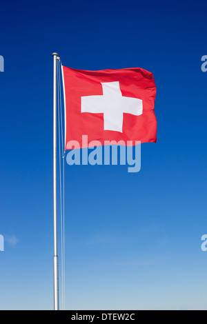 Die Nationalflagge der Schweiz auf einer Metallstange vor einem strahlend blauen Himmel fliegen. Stockfoto