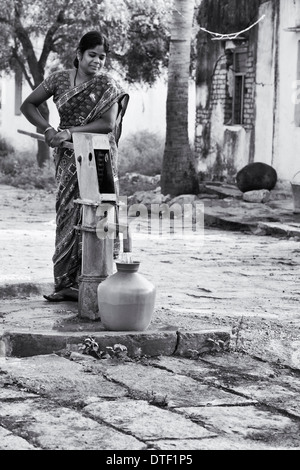 Indische Frau Füllung Kunststoff Wassertopf aus einem ländlichen Dorf Handpumpe. Andhra Pradesh, Indien. Monochrom Stockfoto