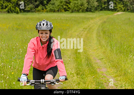 Frau Reiten Fahrrad auf Landschaft Weg durch Wiese lächelnd Stockfoto