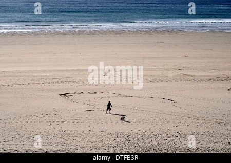 Hundespender/Mann läuft neben seinem Hund an einem menschenleeren Strand in Cornwall. Stockfoto