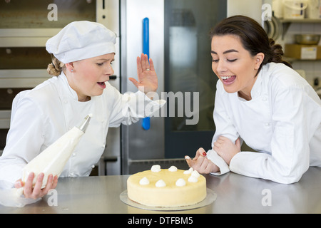 Konditor Lehrling Nibbeln Schlagsahne aus Kuchen in der Bäckerei Stockfoto