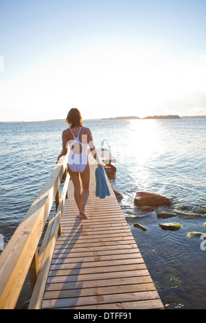 Attraktive Frau in weißen Badeanzug zu Fuß auf Holzmole in Skandinavien im Sommer Stockfoto
