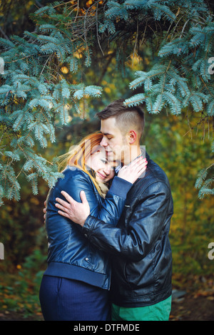Attraktives junges Paar in einem Stadtpark auf einem Hintergrund von Tannen umarmen Stockfoto