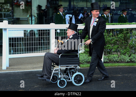 Ascot, Großbritannien, elegant gekleideter Mann einen älteren Mann im Rollstuhl schieben Stockfoto