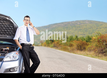 Jungunternehmer am Telefon neben einem Auto auf einer Landstraße Stockfoto