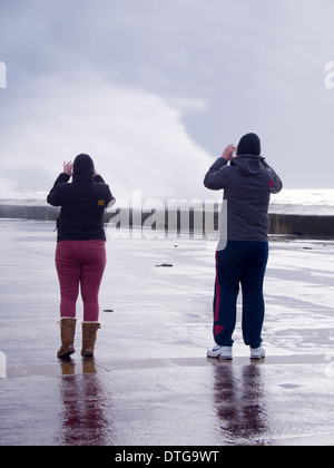 Ein Mann und eine Frau fotografieren die Wellen brechen über die Ufermauer in Southsea, Portsmouth, England. Stockfoto