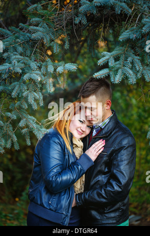 Attraktives junges Paar in einem Stadtpark auf einem Hintergrund von Tannen umarmen Stockfoto