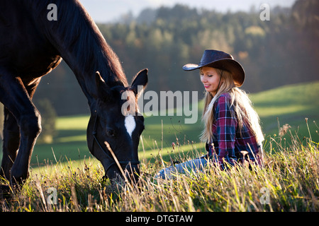 Eine junge Frau mit einem schwarzen Hannoveraner Pferd auf einer Bergwiese im Herbst, Nord-Tirol, Österreich Stockfoto