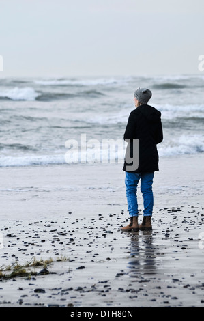 Eine Frau steht am Strand und blickt auf stürmischer See Stockfoto