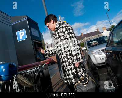 Eine Frau in einem Hahnentritt Muster Stoff Check Mantel, Geld in einen Automaten in einem Supermarkt-Parkplatz UK KATHY DEWITT Stockfoto