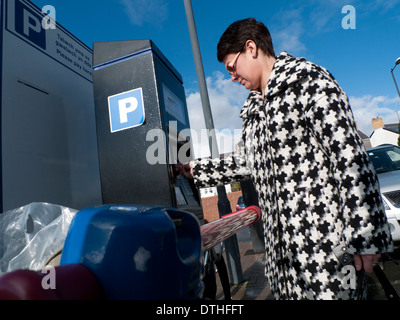 Eine Frau in einem Hahnentritt Muster Stoff Check Mantel, Geld in einen Automaten in einem Supermarkt-Parkplatz UK KATHY DEWITT Stockfoto