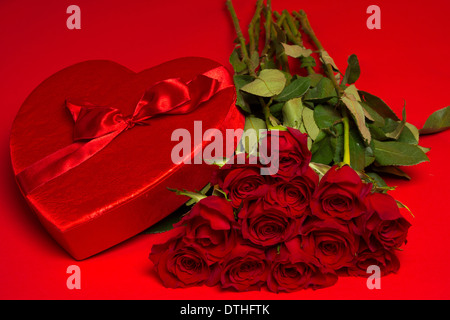 ein Dutzend lange stammten, rote Rosen und ein rotes Herz-Feld auf rotem Grund Stockfoto