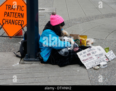 Junge Obdachlose Frau umarmt ihr Hund sitzt auf dem Bürgersteig in der Innenstadt von Vancouver, BC, Kanada Stockfoto