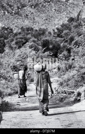 Indische Frauen tragen einen Plastiktopf mit Wasser aus einer Hand-Pumpe in einem indischen Dorf. Andhra Pradesh, Indien. Schwarz / weiß Stockfoto