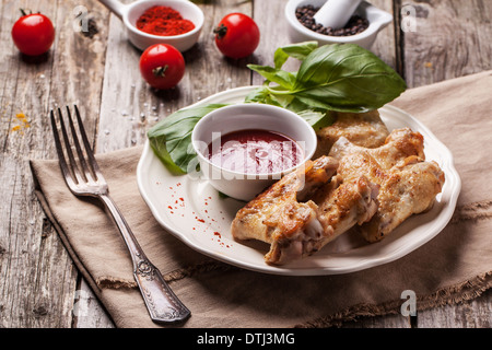 Platte von gegrillte Chicken Wings mit Tomaten tief und frischem Basilikum über alten Holztisch serviert. Stockfoto