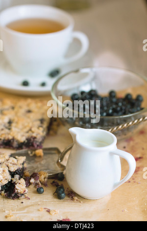 Weiße Krug Milch auf Tisch mit Frühstück mit hausgemachten Heidelbeerkuchen und Schale mit frischen Heidelbeeren Stockfoto