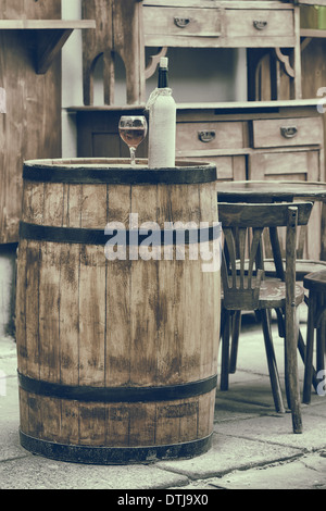 Vintage stilisierte Foto von Holzfass mit Flaschen Wein und Glas, Stuhl und Tisch im Café im freien Stockfoto