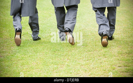 Bräutigam und zwei Trauzeugen in schwarzen Schuhen graue Hosen und morgen-Mäntel zu Fuß entlang einer Wiese Rückansicht England Stockfoto