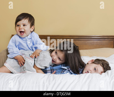 Drei Kinder in einer Familie auf einem großen Bett Pennsylvania USA spielen liegend Stockfoto