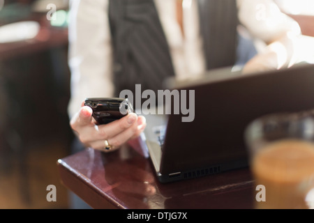 Eine Frau sitzend am Schreibtisch hält ein Smartphone mit einem Laptop-Computer New Hope, Pennsylvania USA Stockfoto