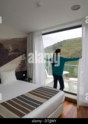 Frau, die aus großen Fenster beim Öffnen der Vorhänge Stockfoto