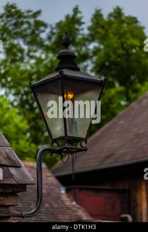 Eine traditionelle viktorianische Gas Licht ein Licht über die Dächer als die Nacht hereinbricht. Die Flamme spiegelt sich in der schmutzigen Glas. Stockfoto