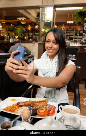 Junge Frau fotografieren Selfie in einem Restaurant beim haben einer englisches gebratene Frühstück, Browns Bar, Cambridge UK Stockfoto