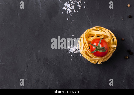 Draufsicht auf trockene Pasta und frischen Kirschtomaten, serviert mit Meersalz auf grauem Schiefer dunkel Stockfoto