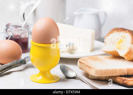 Frühstück mit Eiern und Toast mit Marmelade und Butter auf einer weißen Tischdecke serviert Stockfoto