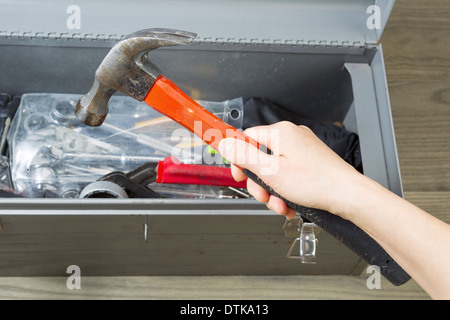 Horizontale Foto von weiblicher Hand unter alten hammer aus Werkzeugkasten mit alten Holzböden im Hintergrund Stockfoto