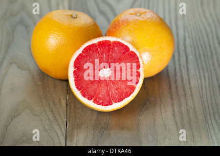 Horizontale Foto von Ruby red Grapefruit geschnitten Hälfte vor zwei ganze Früchte auf Alter Holz Stockfoto