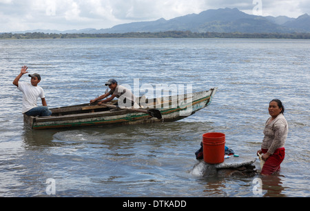 Junge Männer in einem Ruderboot ausgehen am Lago de Apanas, Nicaragua, vorbei an einer Frau Hand Waschen Wäsche Stockfoto