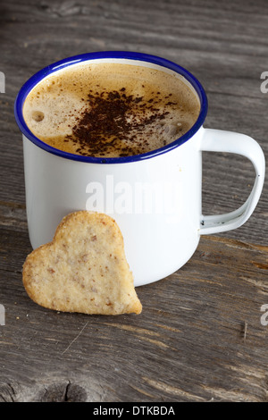 Emaille Becher mit heißem Kaffee und ein Cookie in Herzform auf alten rustikalen Holzbrett mit und textfreiraum unteren Bildbereich Stockfoto