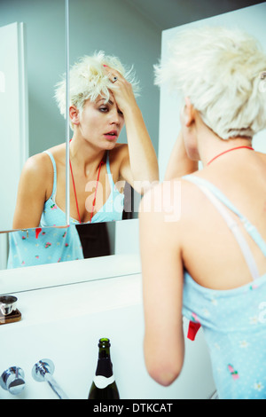 Verkatert Frau prüft sich selbst im Spiegel Stockfoto