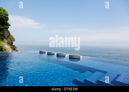 Liegestühle im Infinity-Pool mit Blick auf Meer Stockfoto