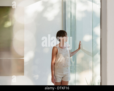 Nachdenkliche Frau am sonnigen Fenster stehen Stockfoto