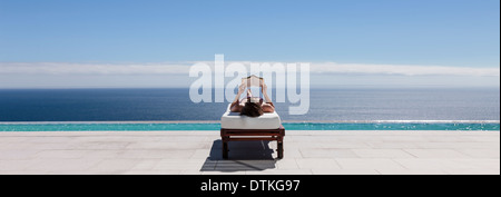 Frau, entspannend auf Liegestuhl am Pool mit Blick auf Meer Stockfoto